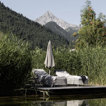 Sonnenliegen auf Holzplattformen am Bergsee des Wellnesshotels Der Engel