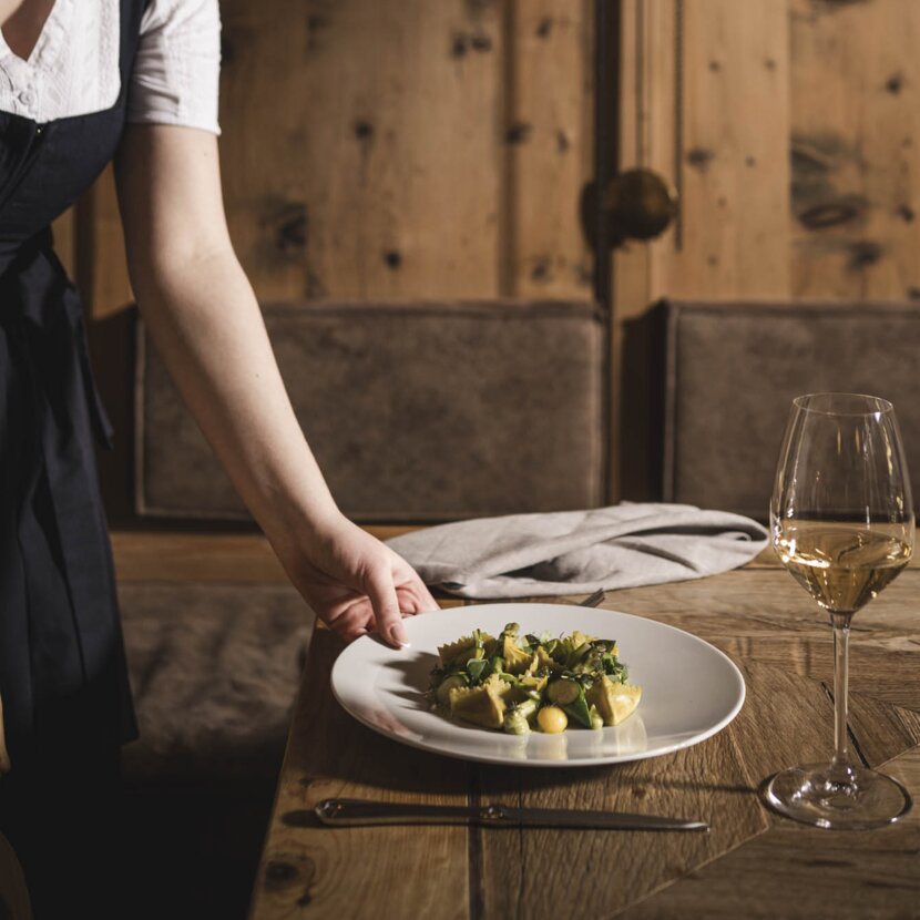 Servicekraft im Dirndl stellt Frühlingshaftes Gericht am alten Holztisch ein