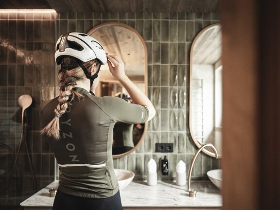 Mountainbikerin im olivgrünen Radoutfit steht vor dem Spiegel im Bad des Orgänic Zimmers