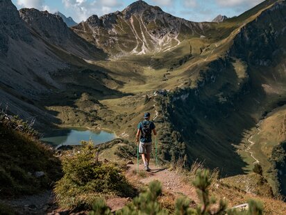 Basti Heckl wandert auf einem Wanderpfad zur Schochenspitze - im Hintergrund die Berglandschaft und ein türkiser See