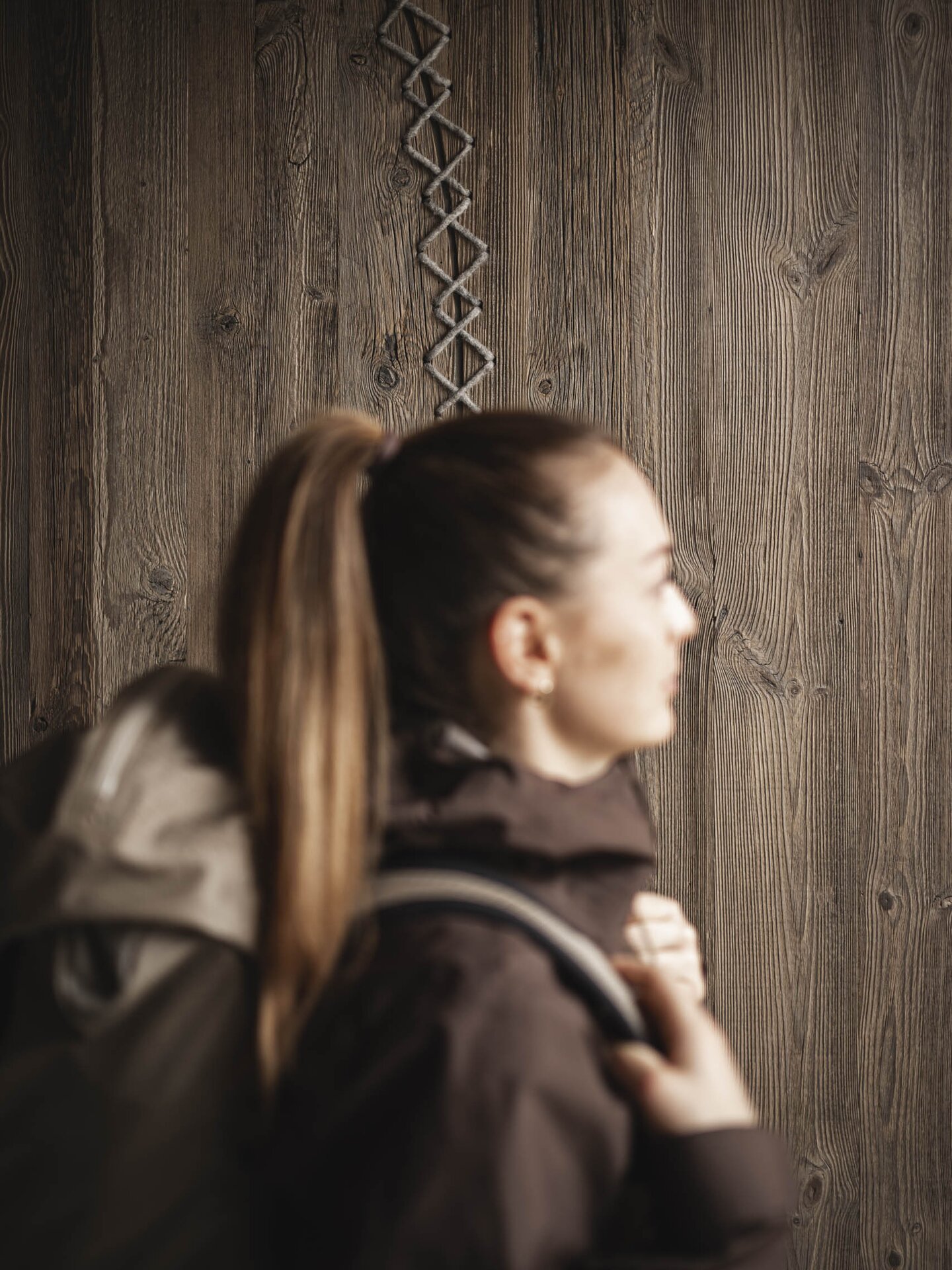 Person mit braunem Wanderrucks und brauner Outdoor-Jacke im Vordergrund - im Hintergrund braune Holzwand - Monochrome Farbwelt