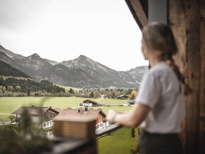 Person steht am Balkon des Zimmers Orgänic Nest mit Ausblick auf die Tannheimer Bergwelt