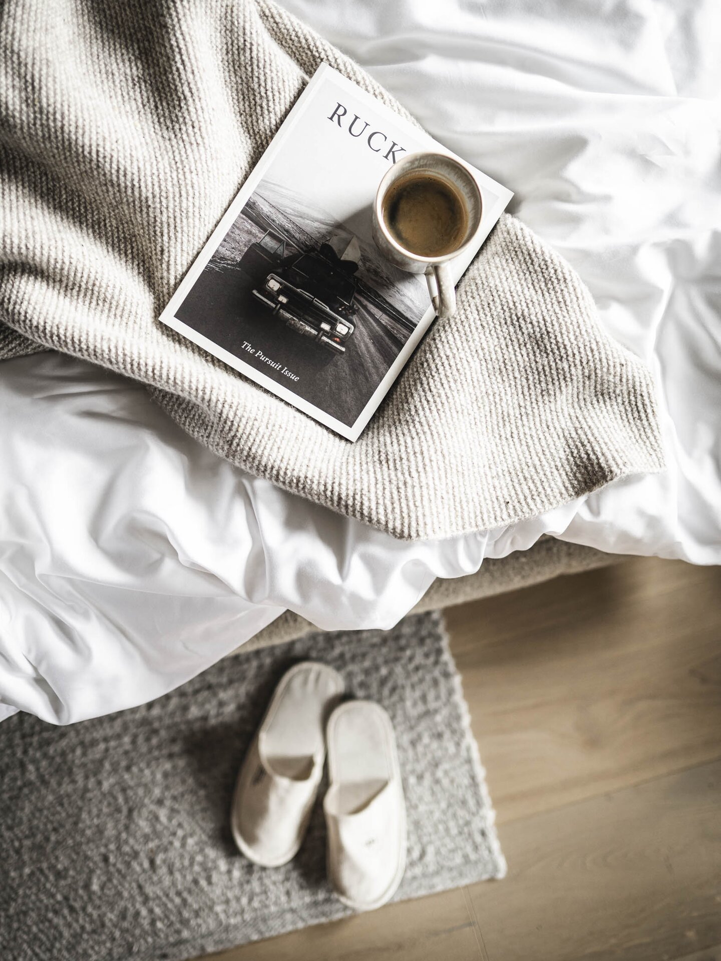 Designer-Bett im Orgänic Top Komfortzimmer Nord mit greiger Tagesbettdecke, einem guten Buch, Kaffee und Orgänic Badeslipper auf dem Boden