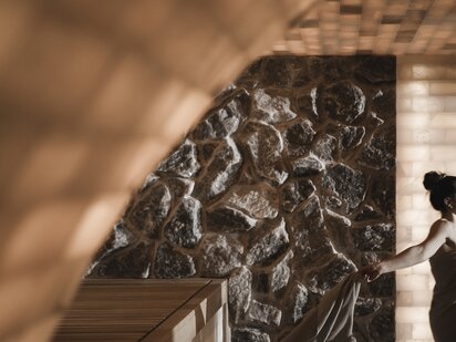 Person in der Sauna vor einer Natursteinwand im Orgänic Spa